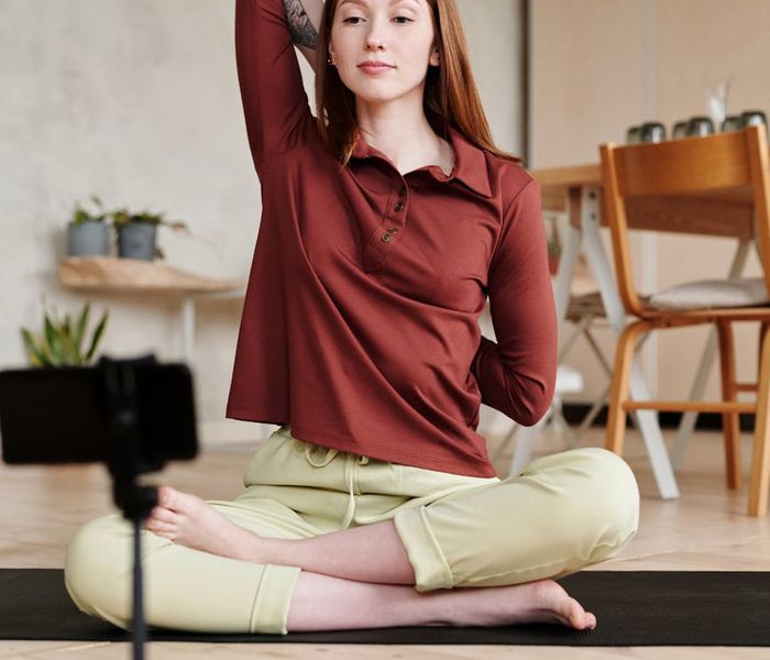 Smiling woman stretching on a yoga mat with a plant in the background.